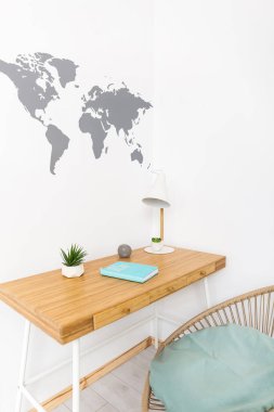 Scandi tarzında beyaz ve ahşap parlak çalışma alanı. Lambalı ve defterli şık bir masa, modern rattan sandalye, beyaz bir duvarda dünya haritası.