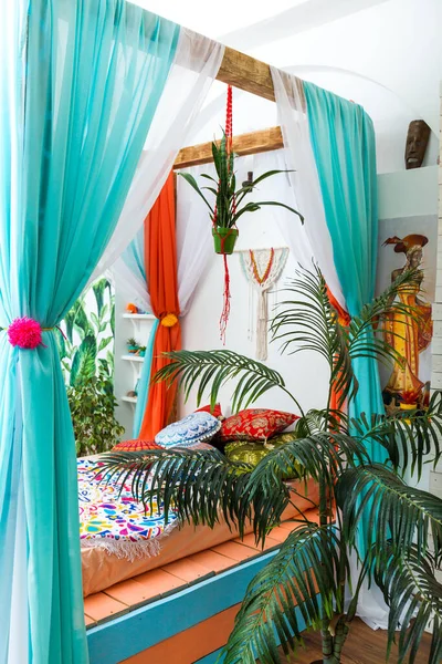 Marrakech bedroom in bright colors with home plants. Bed with curtains, colorful pillows.