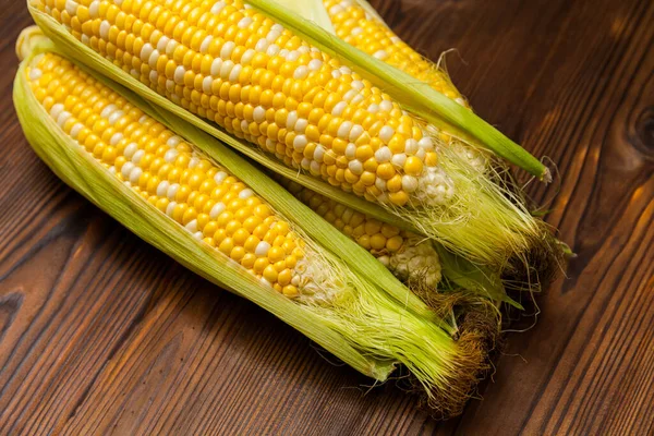 Fresh sweet corn on cobs on wooden table, closeup, top view. Fresh yellow corns ears with leaves. Ears of freshly harvested yellow sweet corn on wooden table.