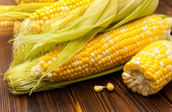 Fresh sweet raw corn on cobs with leaves on wooden table, closeup, top view. Fresh yellow corns ears with leaves. Ears of freshly harvested yellow sweet corn on wooden table.