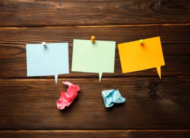 Kağıt renkli konuşma baloncukları, kağıt yapışkan bulut şekilli çıkartmalar ve ahşap arka planda buruşmuş kağıt toplar.