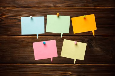 Kağıt renkli konuşma baloncuklarıyla şekil verin, tahta arka planda kağıt gibi yapışkan bulut şekilli çıkartmalar