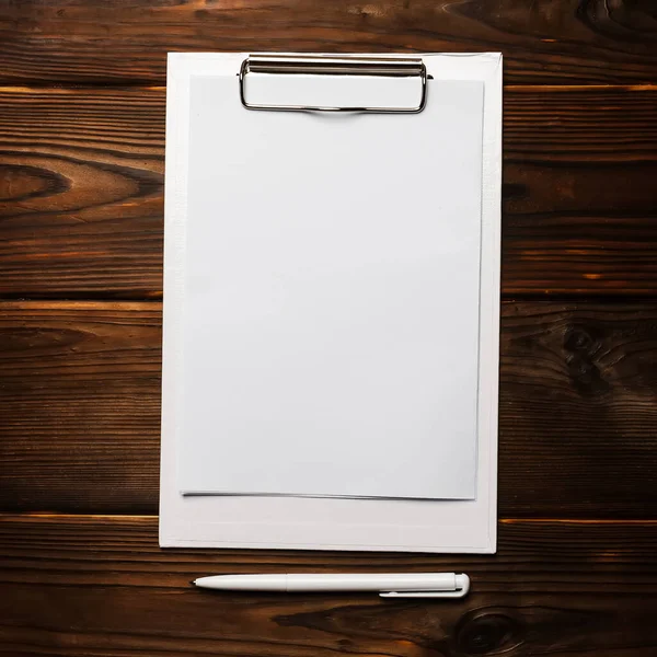 Tahta arka planda beyaz kalem ve boş bir kağıt ile beyaz bir pano. Üst görünüm ofis aksesuarları