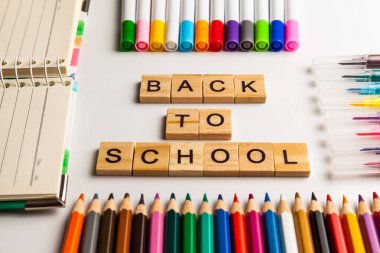 Okul malzemeleri, çok renkli kalemler, defter ve kalemler masanın üstünde. Tahta bloklardan yapılmış okul metnine geri dön