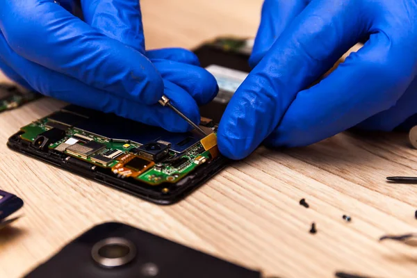 The technician repairing the smartphone\'s motherboard in the workshop on the table. Concept of computer hardware, mobile phone, electronic, repairing, upgrade and technology.