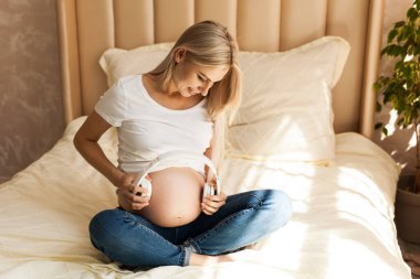 gebelik, teknoloji ve insan konsepti - mutlu hamile kadın doğum öncesi müzik uyarımı için kulaklıklarını karnına uyguluyor