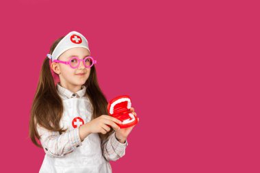 Oyuncak çenesi ve pembe arka planda diş fırçası olan tıbbi kıyafetli küçük havalı doktor dişçi kız.