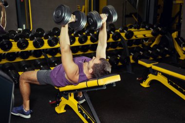 Erkek sporcu spor salonunda halterlerle ağırlık kaldırıyor.