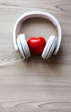 Tahta masanın ortasında kırmızı kalp işareti olan beyaz kulaklıklar. Müzik konseptini seviyorum
