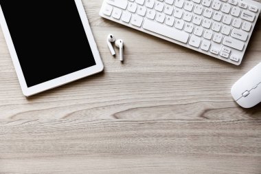 Ofis masası düz görünüm ile klavye, fare, tablet bilgisayar ve kablosuz kulaklık ahşap doku arka planı.