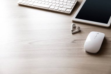 Ofis masası düz görünüm ile klavye, fare, tablet bilgisayar ve kablosuz kulaklık ahşap doku arka planı.