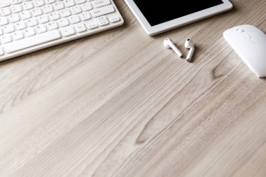 Ofis masası düz görünüm ile klavye, fare, tablet bilgisayar ve kablosuz kulaklık ahşap doku arka planı.