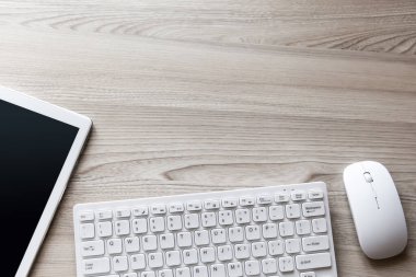 Beyaz tablet tablet, kablosuz kulaklık, fare ve klavye ile ahşap çalışma yüzeyi. Kopyalama alanı olan üst görünüm. Düz yatıyordu.