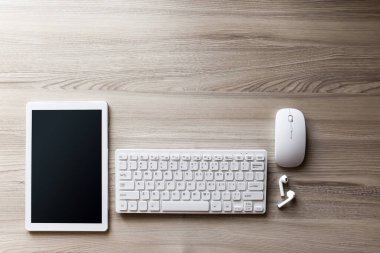 Ofis masası düz görünüm ile klavye, fare, tablet bilgisayar ve kablosuz kulaklık ahşap doku arka planı.