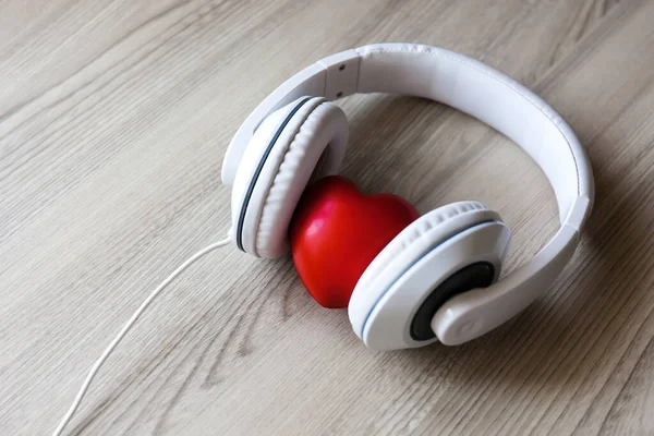 Tahta masanın ortasında kırmızı kalp işareti olan beyaz kulaklıklar. Müzik konseptini seviyorum
