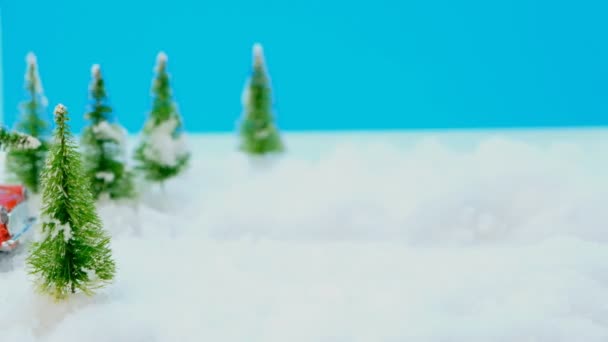 红色的玩具车 屋顶上挂着一棵圣诞树 在雪地的森林里驰骋 雪花飘落 田野浅薄 蓝天蔚蓝 — 图库视频影像