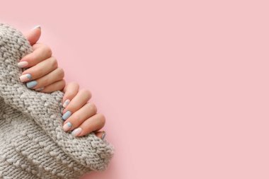 Kadın eli manikürlü. Pembe arka planda örülü süveter var. Moda Geometrik Tırnak Sanatı Manikürü. Manikür salonu afişi