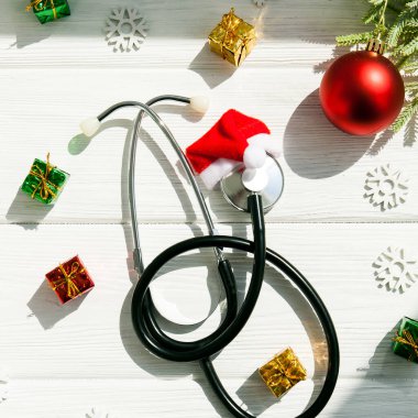 Noel Baba şapkalı steteskop ve tahta beyaz masa üzerindeki Noel süslemeleri. Tıbbi konsept. Tebrik kartı. Yeni Yıl ve Noel.