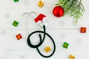 Noel Baba şapkalı steteskop ve tahta beyaz masa üzerindeki Noel süslemeleri. Tıbbi konsept. Tebrik kartı. Yeni Yıl ve Noel.