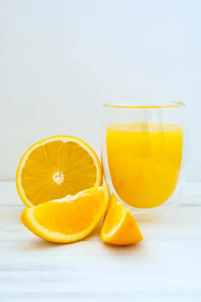 orange juice and orange cut into slices and wedges on white wooden background.