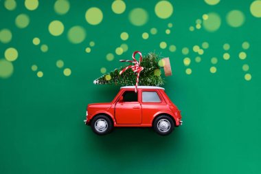Noel 'i ya da yeni yıl tebrik kartını kutlamak için minimum tasarım. Hediye teslimi konsepti. Küçük kırmızı oyuncak araba ve yeşil arka planda Noel ağacı.
