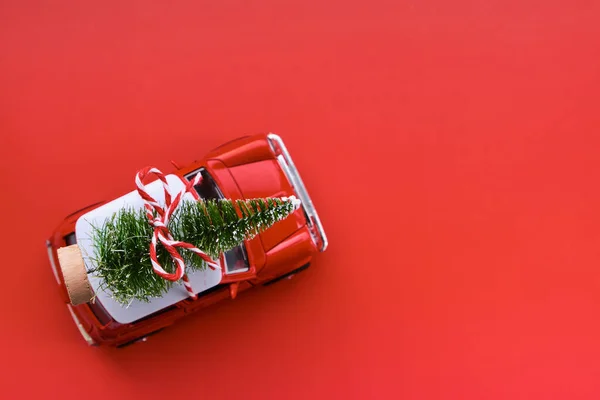 庆祝圣诞节或新年贺卡的最小设计 送礼的概念 红色背景上的红色小玩具车和圣诞树 有复制空间 — 图库照片