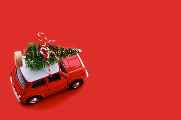 Red small retro toy car with gift on the roof on red background. Delivery. New Year and Christmas, Sale concept.