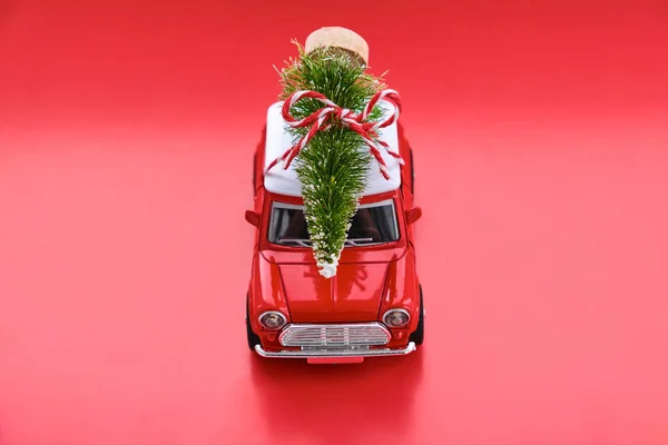 Red small retro toy car with gift on the roof on red background. Delivery. New Year and Christmas, Sale concept.