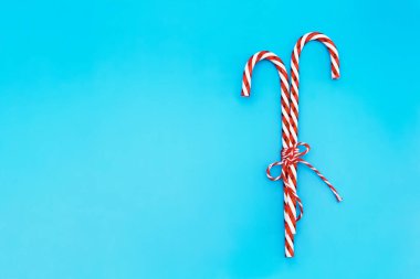 Çizgili halat yaylı Noel şeker kamışları mavi arka planda, kar taneleriyle izole edilmiş. Tatlı Noel kartı kopyalama alanı