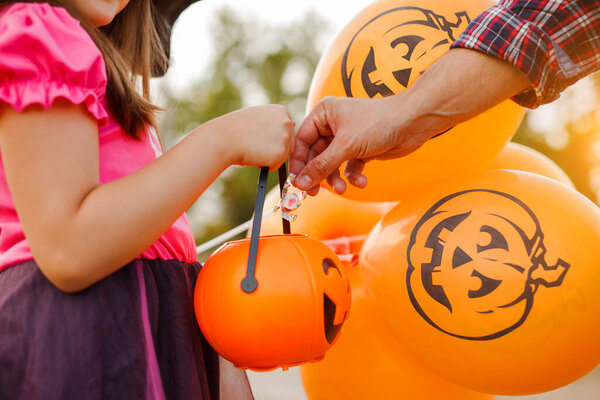 Little kid girl trick or treating on Halloween. man's hand puts a candy in the basket