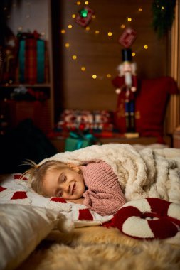 Tatlı kız uykusunda huzur içinde gülümsüyor, ışıldayan ışıklarla dolu bir odada battaniyenin altına kıvrılıp yatıyor. Noel arifesinin büyülü beklentisi, çocukluk hayalleri ve tatilin sıcaklığı