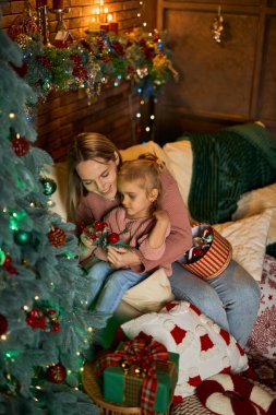 Sevgi dolu anne ve küçük kızı, Noel ağacını samimi ve şenlikli bir odada birlikte süsler. Sıcak ışıklarla dolu sahne, hassas bir aile tatili anını yakalıyor.