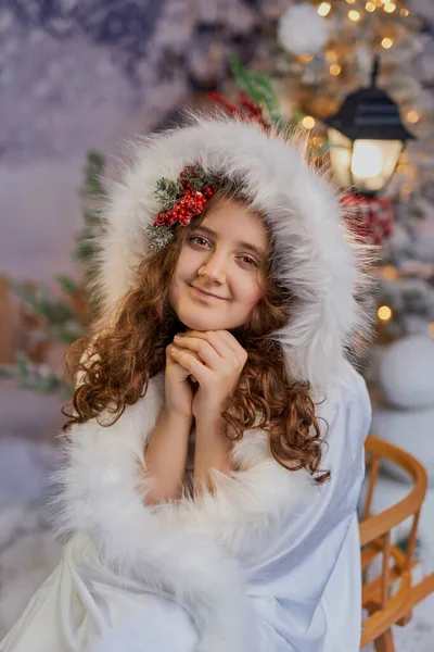 Beyaz kürklü, neşeli böğürtlenli, Noel ortamında oturan neşeli bir kızın portresi. Bayram kartları, kış temaları ve mevsimlik pazarlama için mükemmel.