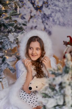 Beyaz kürk desenli pelerinli çekici kız, bir Noel stüdyosunda poz veriyor. Tatil promosyonları ve mevsimlik dekorlar için karlı ağaçların olduğu büyülü kış ortamı.