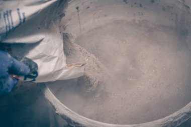 İşçi sıva çantasından bir kova su ile bir mikser karıştırma için içine dökülen