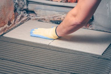 Kiremitçi kabuk ve sarı eldiven elinde bir kare taşı yere giderir.