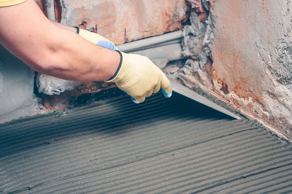 The worker carefully puts the square tile on the floor