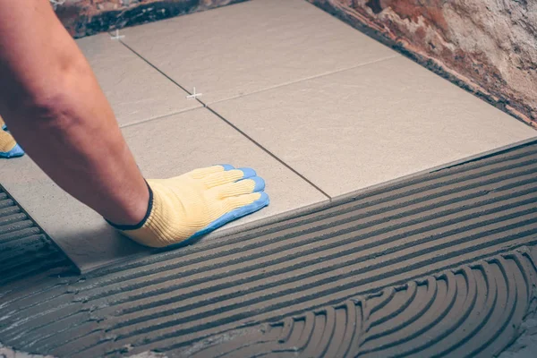 The worker professionally puts the tile on the floor, tiling the bathroom