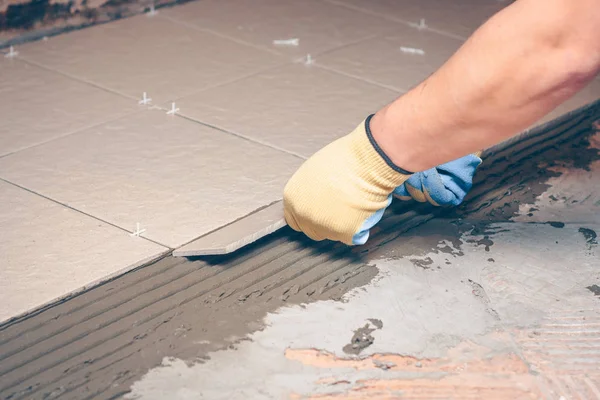 The worker\'s hands mount the tile on the floor