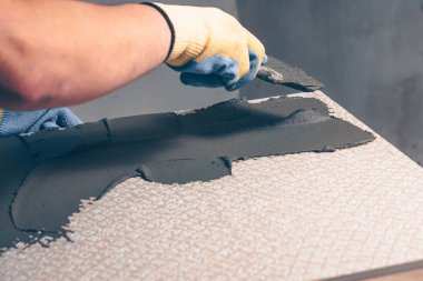 Çalışma kiriş eli bir spatula ile seramik döşemenin arkasına bir tutkal koyar