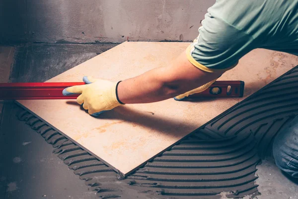 Worker finisher checks the quality of tile works on the floor with the help of a building level, highly skilled work