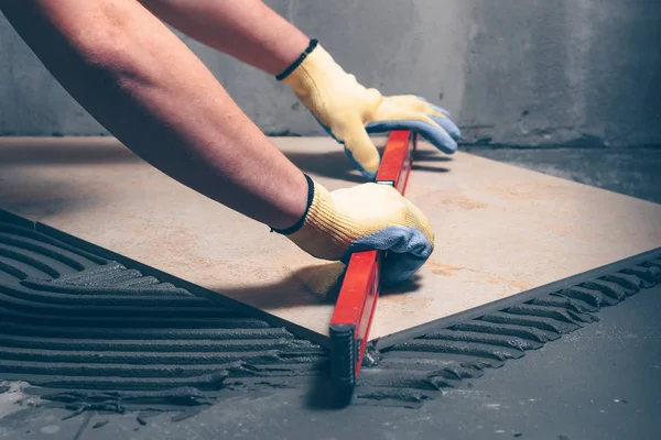 Worker finisher checks the quality of tile works on the floor with the help of a building level, highly skilled work