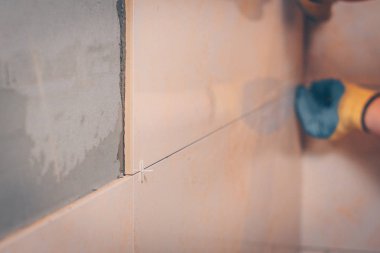 Çalışan ustalar duvardaki fayansları nemli bir süngerle siler. Bağlantı dikişinden tutkal kalıntılarını çıkarır. Odaklanamaz.