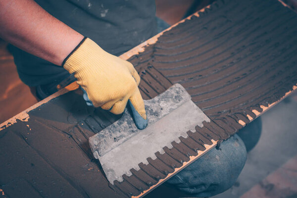 The working tiler applies glue on the tile with a notched trowel before gluing, the technology of tiling and finishing