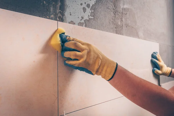 The working tiler wipes the tiles after laying, the professional highly skilled technology of tiling and finishing