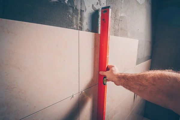 The working tiler checks the laying of tiles with the help of a building level, a first-person view, a professional highly skilled tile laying technology and finishing