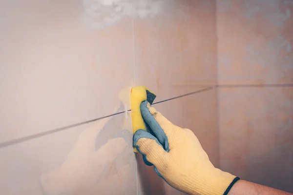 The working tiler wipes the tiles after laying, the professional highly skilled technology of tiling and finishing