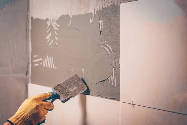 The working tiler applies glue on the wall with a spatula before gluing, the technology of tiling and finishing
