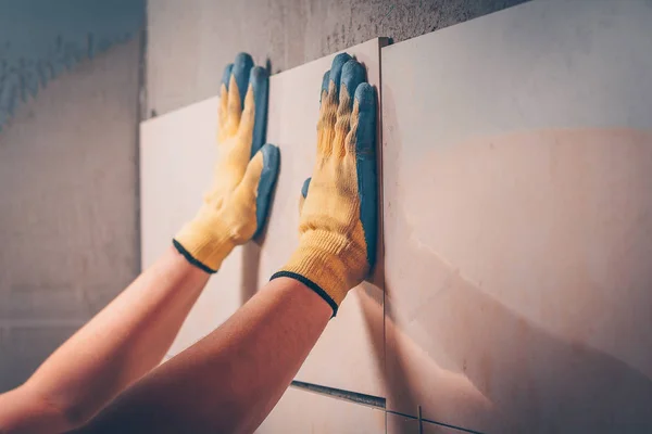 The working tiler puts the tiles on the wall, adjusts the position of the freshly glued tiles by hand, unfocused, the technology of tiling and finishing
