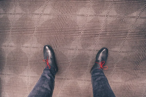 The legs of a man in shoes with red laces on the carpet, a fashionable man in jeans